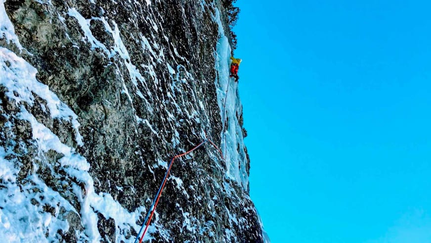 An steiler Eiswand klettert Bergführer Tommaso Cappelletto in roter Jacke mit Eisgeräten, gesichert über rotes Seil.