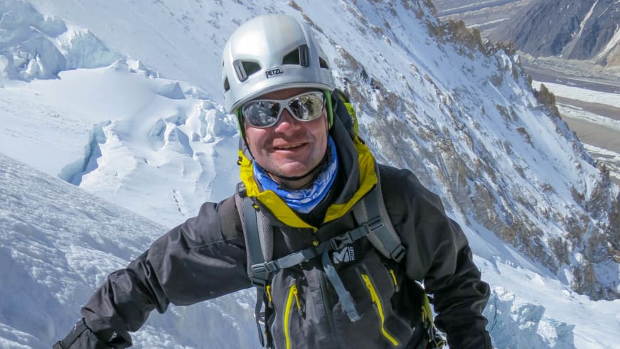 Portrait von Bergführer Tadej Zorman mit weißem Kletterhelm und Gletscherbrille vor verschneiter Bergkulisse mit Seracs und Spalten.