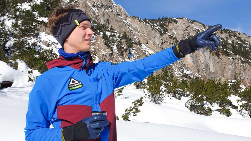 Bergwanderführer Uwe Roth in blau-roter Winterjacke zeigt mit ausgestrecktem Arm den Weg und hält eine Thermoskanne in der Hand.