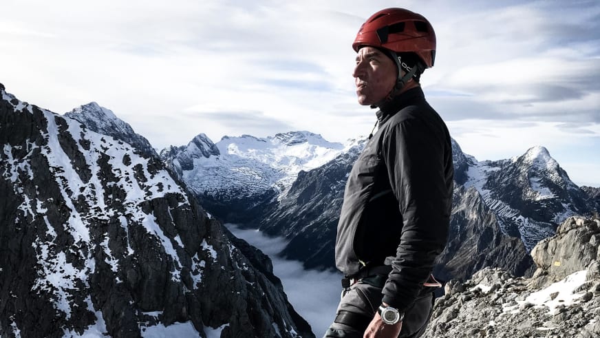 Bergwanderführer Helmut Freyer mit rotem Helm steht auf exponiertem Felsgrat über Wolkendecke im Winter.