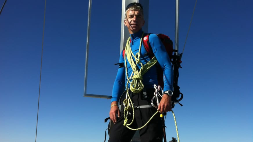 Bergwanderführer Helmut Freyer steht in kompletter Kletterausrüstung mit gelbem Seil um die Schultern vor blauem Himmel.