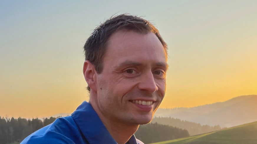 Portrait von Bergwanderführer Markus Radinger in blauer Outdoor-Jacke vor hügeliger Landschaft bei warmem Abendlicht.