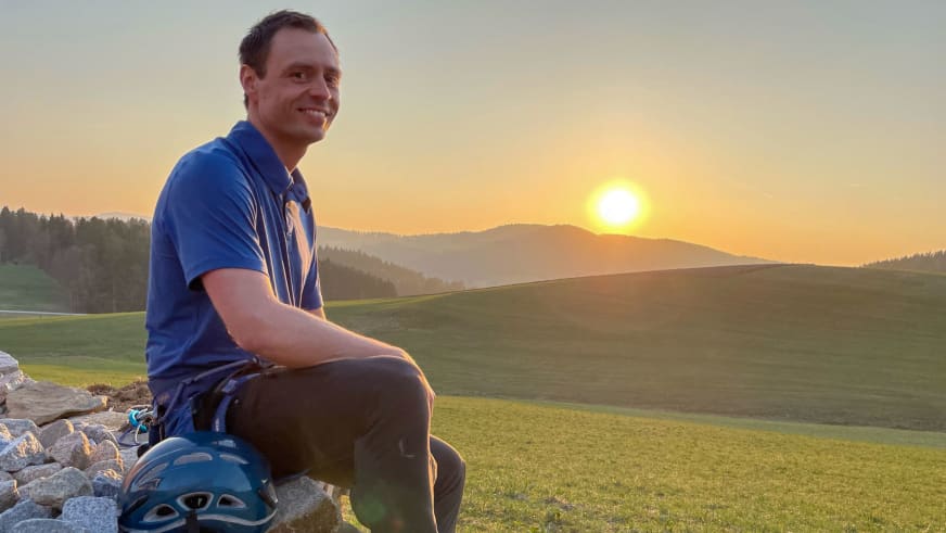 Bergwanderführer Markus Radinger in blauem Poloshirt sitzt auf Steinblock mit Klettergurt und blauem Helm.