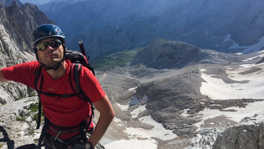 Bergwanderführer Markus Radinger in roter Funktionsjacke und schwarzem Klettergurt auf Felsvorsprung im Hochgebirge.