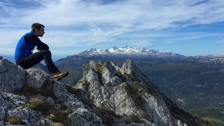 Bergwanderführer Markus Radinger in blauer Jacke sitzt entspannt auf Felsvorsprung mit Blick auf Bergpanorama.
