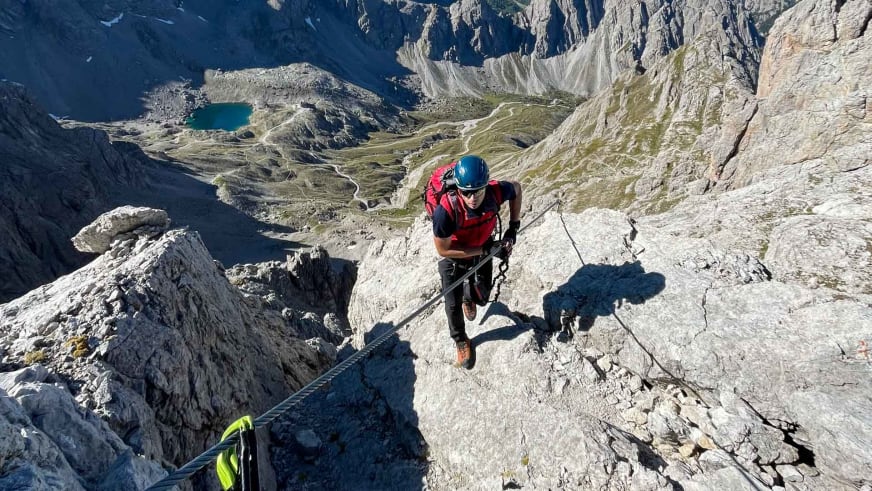 Aufnahme von oben zeigt Bergwanderführer Markus Radinger in roter Kleidung am steilen Kalkfels über türkisblauen Bergseen.
