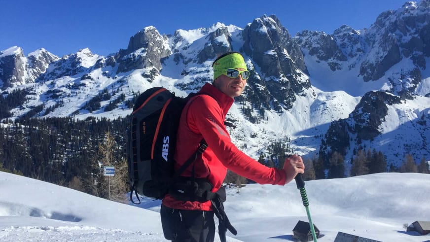 Bergwanderführer Markus Radinger in roter Skijacke mit grüner Mütze und Sonnenbrille vor verschneiter Bergkulisse.