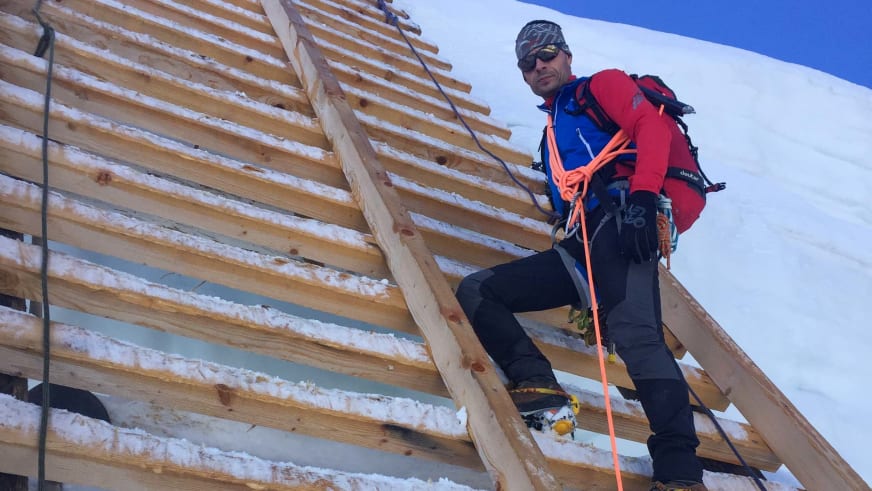 Bergwanderführer Markus Radinger in roter Ausrüstung und dunklem Helm steht auf Holzdach eines Gebäudes im Bau.