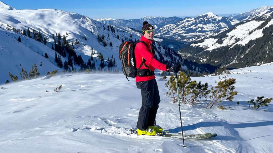 Bergwanderführer Markus Radinger steht mit Tourenski auf verschneitem Plateau zwischen Latschen vor Bergpanorama.