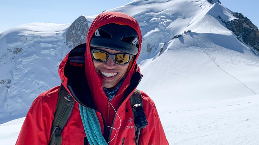 Portrait zeigt Bergführer José Salazar mit roter Kapuzenjacke und türkisfarben Kletterseil vor verschneiter Berglandschaft.