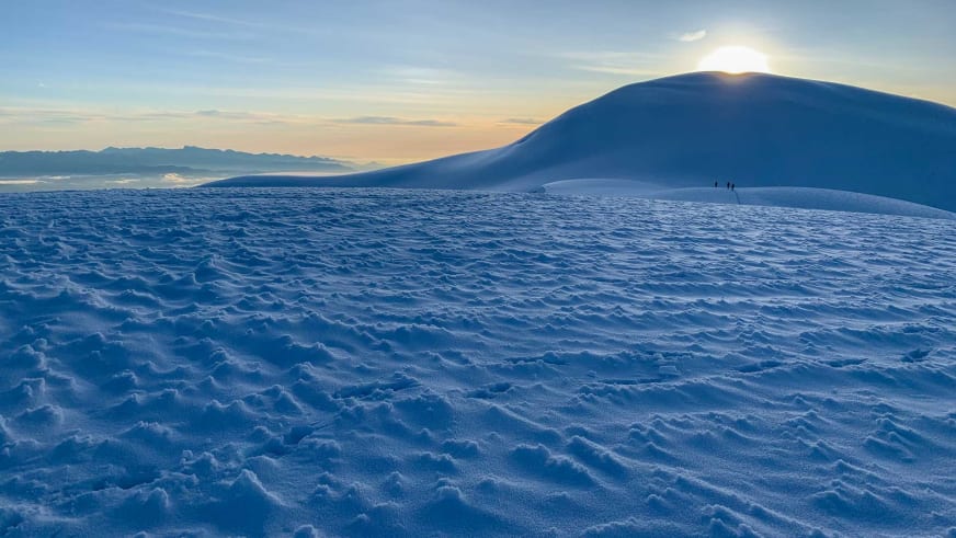 Weitläufige Schneefläche in Dämmerungsstimmung mit Bergführer José Salazar und Begleiter als kleine Figuren am rechten Bildrand.