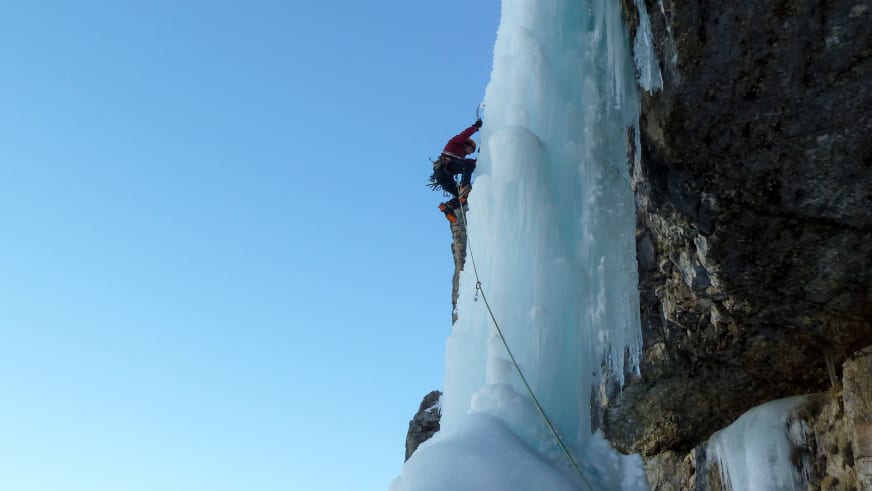 An einer steilen Eiswand klettert Bergführer Davide Marinovich in roter Winterjacke mit Helm und Eisgeräten gesichert am Seil.