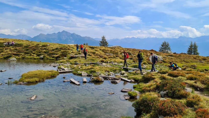 Bergwanderführer Christoph Knappe führt eine Wandergruppe über ein Hochplateau mit klarem Gebirgssee und Bergkette im Hintergrund.