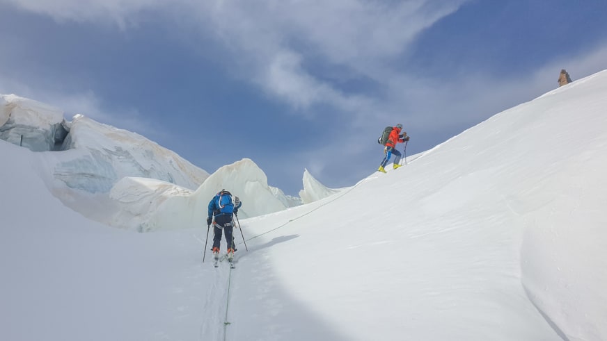 Zwei angeseilte Personen mit Skiausrüstung steigen über steilen Firn auf, Bergwanderführer Christoph Knappe in blauer Jacke führt die Tour.