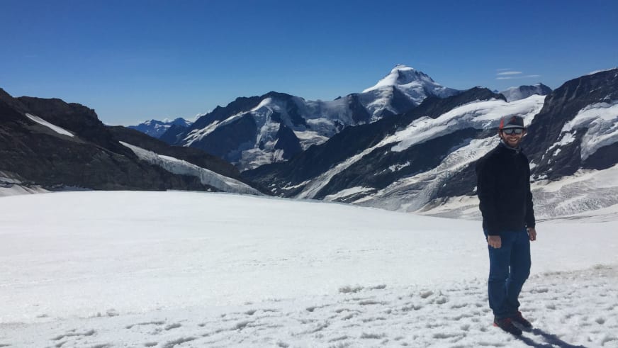 Bergwanderführer Bas Pijpers steht mit rotem Helm auf weiter Gletscherfläche mit schneebedeckten Gipfeln im Hintergrund.