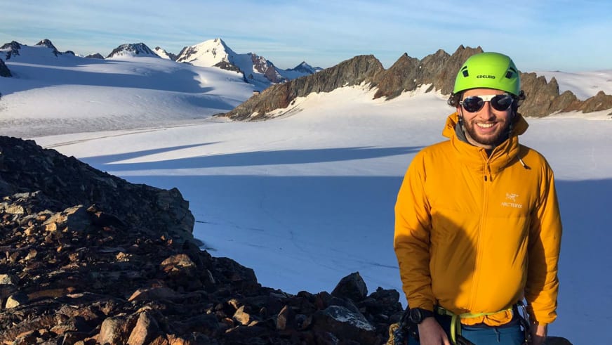 In orangefarbener Arc'teryx-Jacke und grünem Helm steht Bergwanderführer Bas Pijpers lächelnd vor Gletscherlandschaft.