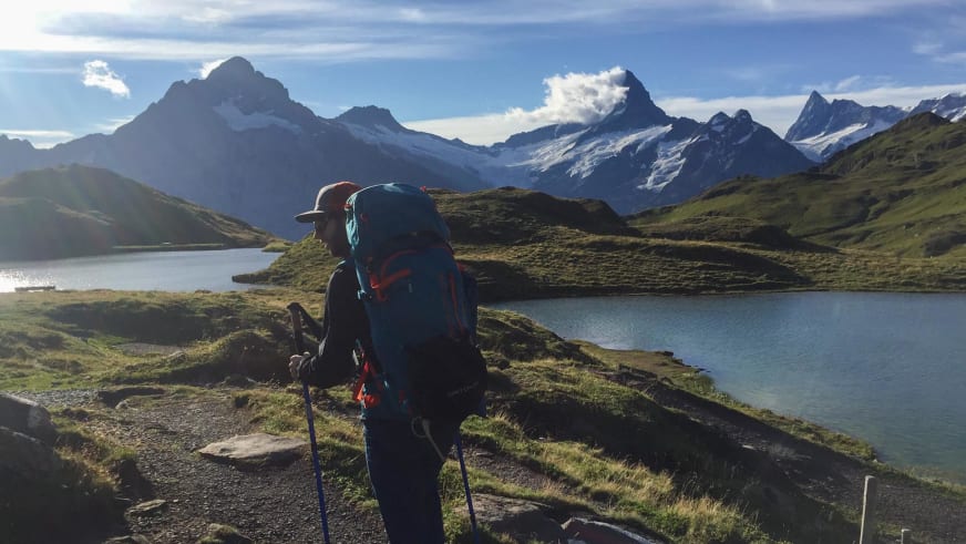 Mit Rucksack und Wanderstöcken geht Bergwanderführer Bas Pijpers auf Schotterweg bergab, vorbei an einem kleinen Bergsee.