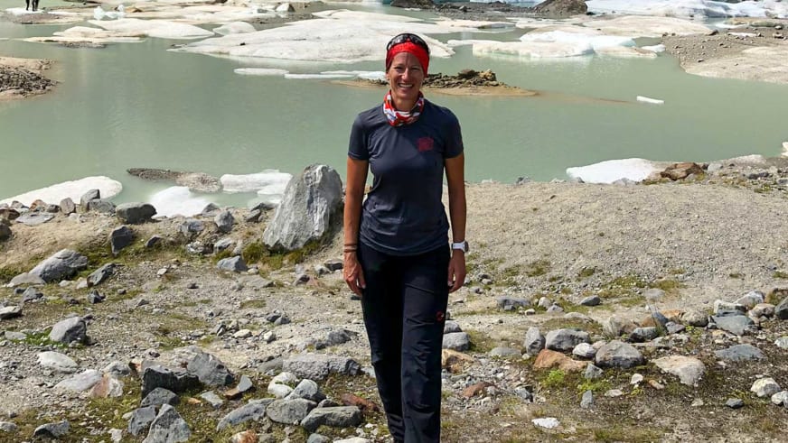 Vor einem Gletschersee mit Eisschollen steht Bergwanderführerin Alexandra Querl in dunkler Funktionskleidung und rotem Stirnband.