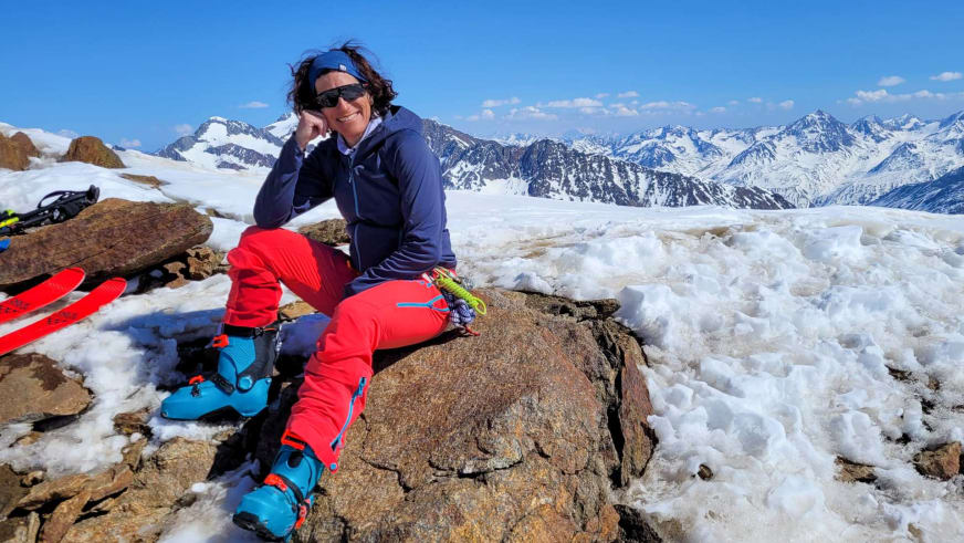 Bergwanderführerin Alexandra Querl sitzt entspannt auf einem Felsblock während einer Skitour in verschneiter Berglandschaft.