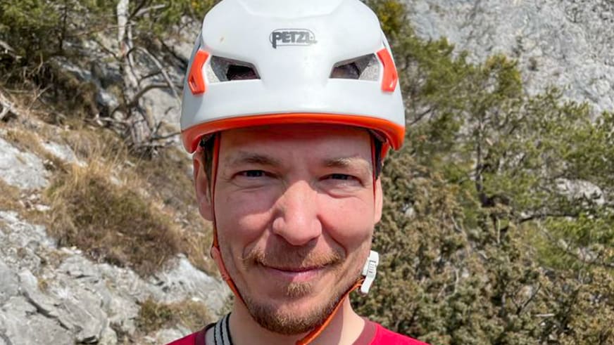 Bergführer Márk Salamon trägt weißen Petzl-Helm mit orangen Akzenten und lächelt in die Kamera.