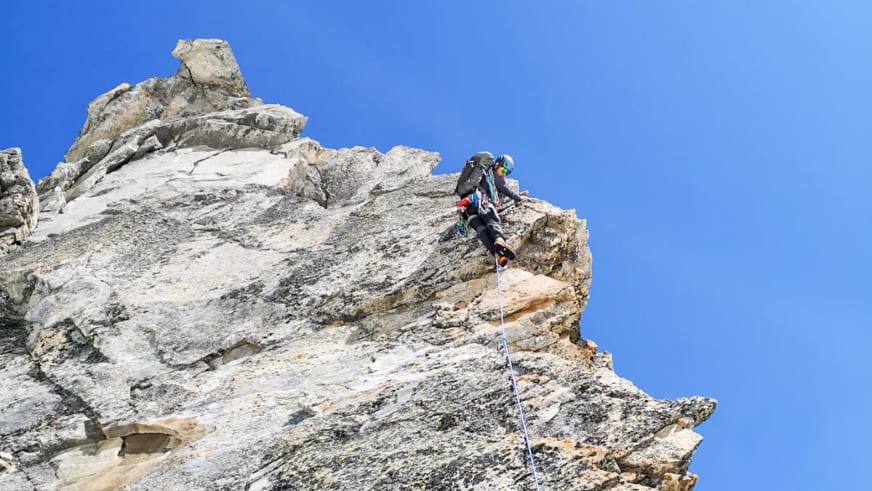 Bergführer Tobias Riedlsperger in schwarzer Kleidung klettert vertikal an hellgrauer Kalkstein-Felswand unter blauem Himmel.
