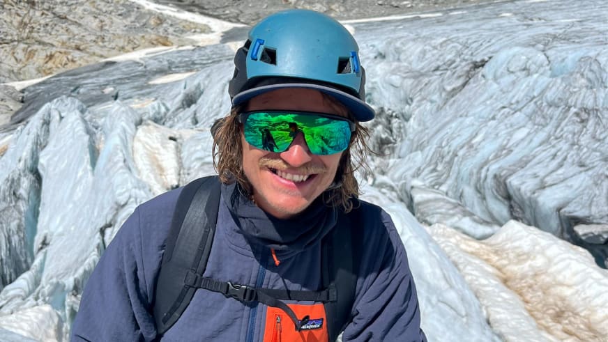 Am Gletscher lächelt Bergführer Tobias Riedlsperger mit blauem Helm in die Kamera, im Hintergrund zerklüftete Gletscheroberfläche.