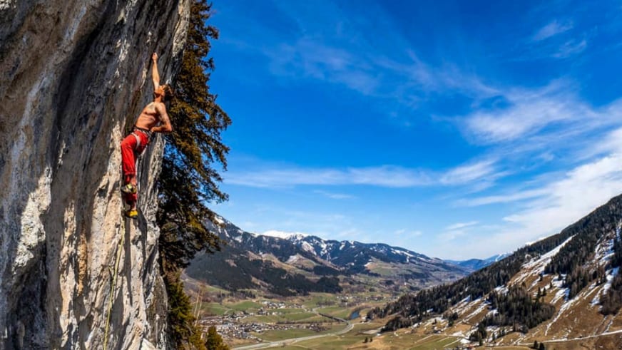 In roter Hose klettert Bergführer Tobias Riedlsperger an senkrechter Kalkstein-Wand über grünem Bergtal.