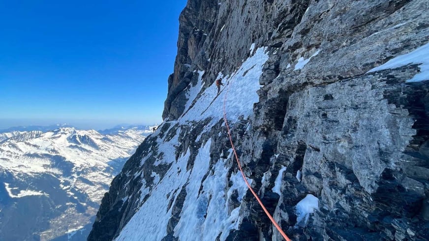 An verschneiter Nordwand klettert Bergführer Tobias Riedlsperger am orangefarbenen Seil über verschneite Berglandschaft.