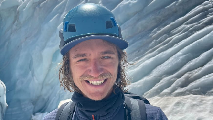 Portrait zeigt Bergführer Tobias Riedlsperger lächelnd mit blauem Helm vor geschichteten Eisformationen.