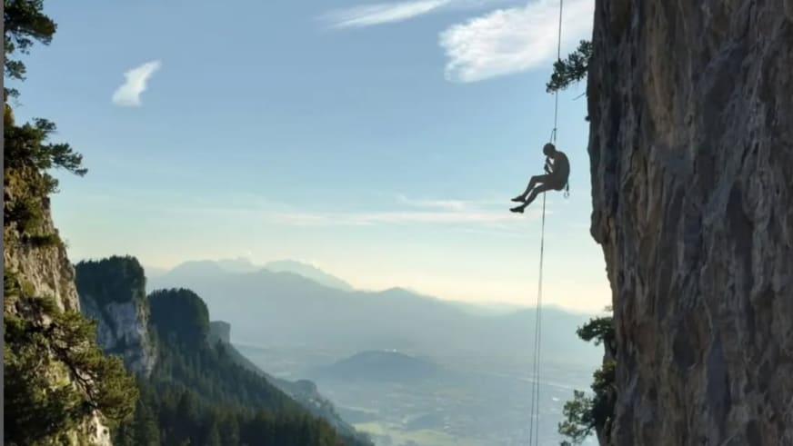 Bergwanderführer Julian Götz hängt am Seil während einer Abseilpause an einer steilen Felswand mit Bergkulisse.