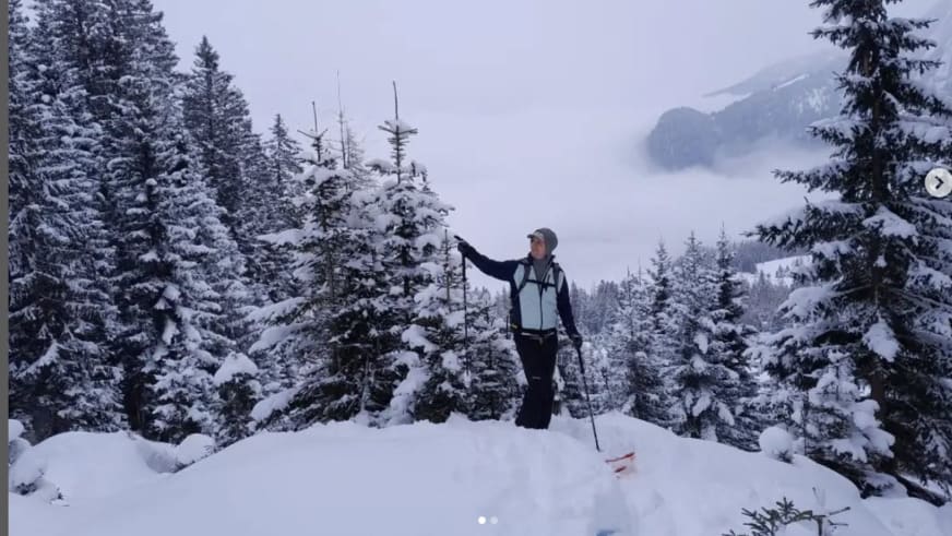 Bergwanderführer Julian Götz steht mit roten Tourenskiern zwischen verschneiten Nadelbäumen im tiefen Pulverschnee.