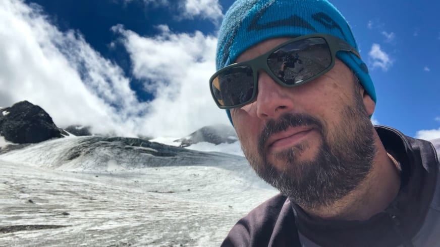 Bergwanderführer Thomas Ziegler mit türkiser Mütze und Sonnenbrille in verschneiter Berglandschaft bei strahlendem Sonnenschein.