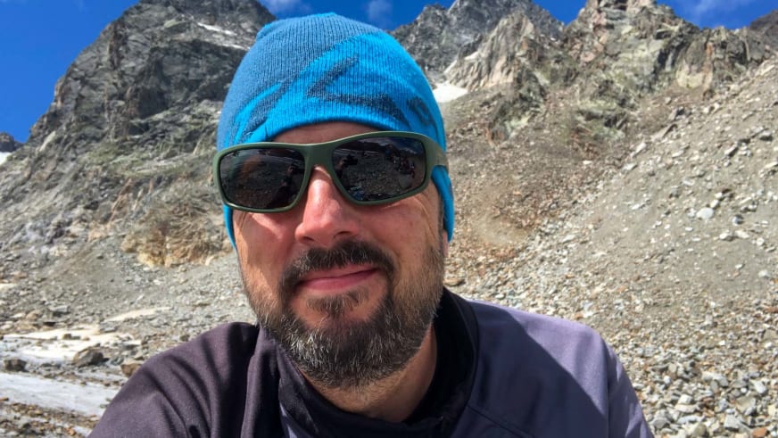 Mit blauer Strickmütze und Sonnenbrille steht Bergwanderführer Thomas Ziegler vor steilen grauen Felswänden.