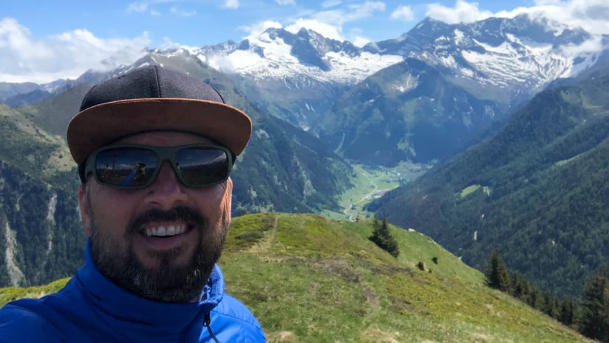 Auf einem grasbewachsenen Bergrücken macht Bergwanderführer Thomas Ziegler ein Selfie vor schneebedeckten Alpengipfeln.