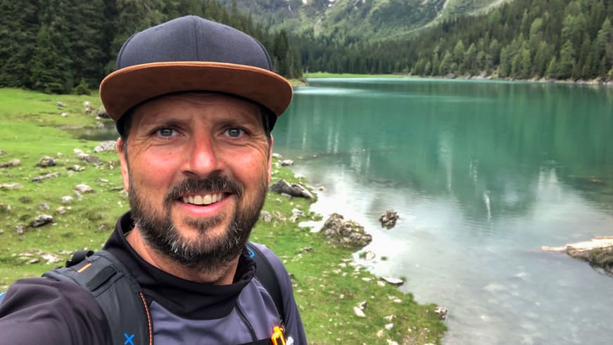 Bergwanderführer Thomas Ziegler macht ein Selfie vor einem türkis-grünen Bergsee mit bewaldeten Hängen im Hintergrund.