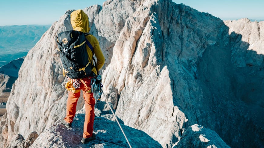 Person in gelber Jacke und oranger Hose steht auf Felsvorsprung in steiler Kalksteinschlucht - Bergführer Enrico Trapazzo führt.