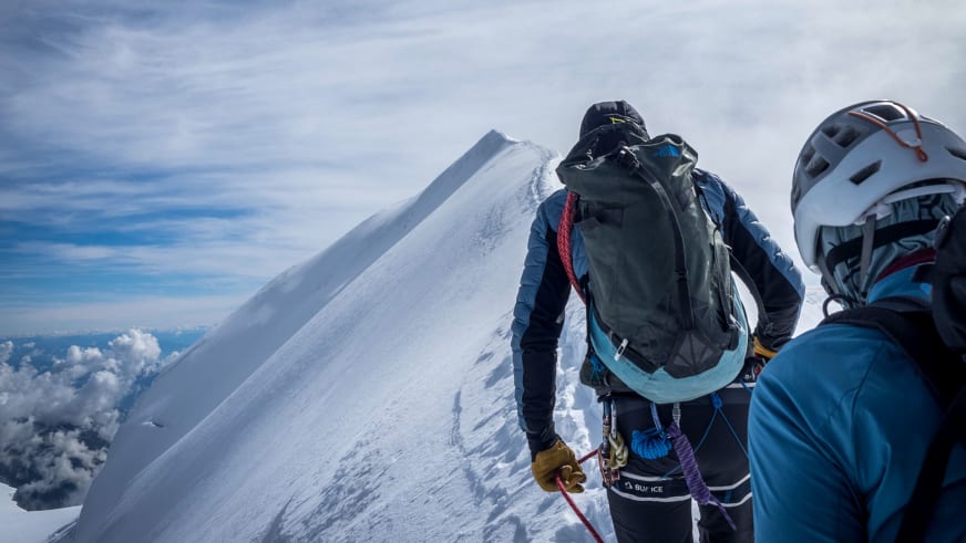 Zwei Bergsteiger bewegen sich angeseilt auf einem schmalen, verschneiten Grat oberhalb der Wolken - Bergführer Enrico Trapazzo führt die Tour.