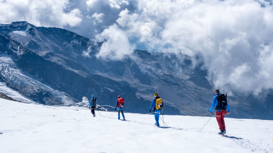 Vier Personen gehen angeseilt mit Skiern über verschneiten Gletscher vor Bergwand - Hochtour mit Bergführer Enrico Trapazzo.