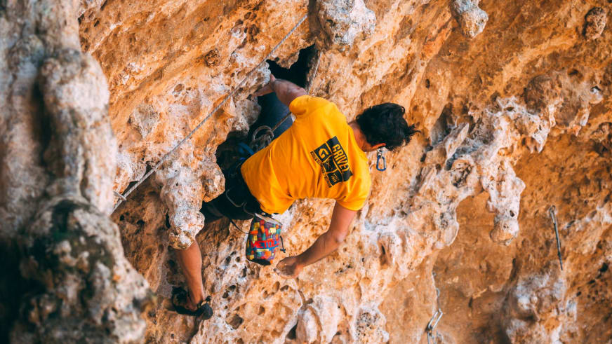 Person in gelbem T-Shirt klettert an überhängender Kalksteinwand - Kletterroute mit Bergführer Enrico Trapazzo.