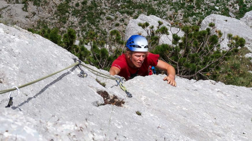 Bergführer Fabian Bendlin klettert in rotem Shirt und blau-weißem Helm an vertikaler Kalksteinwand.
