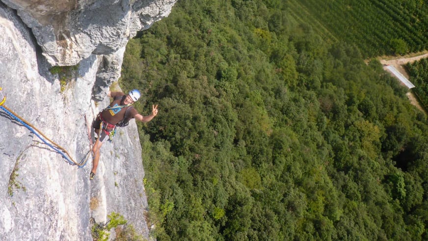 Luftaufnahme zeigt Bergführer Fabian Bendlin beim Freiklettern an steiler Kalksteinwand über bewaldetem Tal.