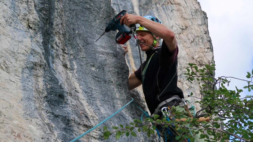 Bergführer Fabian Bendlin führt mit Bohrhammer Wartungsarbeiten an grauer Kalkfelswand durch.