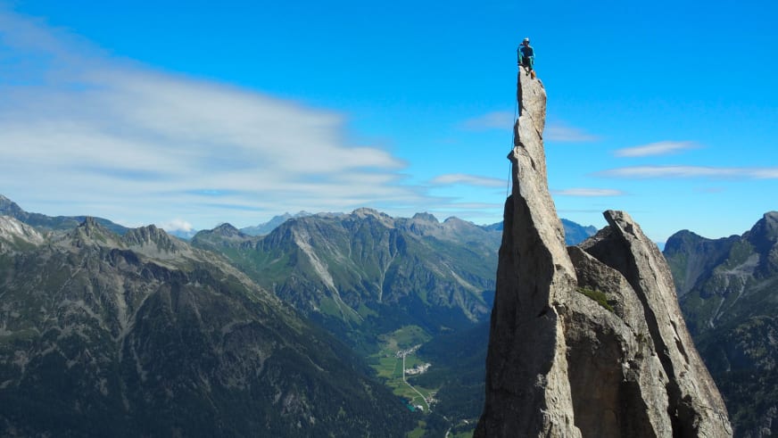 Bergführer Fabian Bendlin steht auf der Spitze einer hohen Felsnadel und blickt über Bergpanorama.