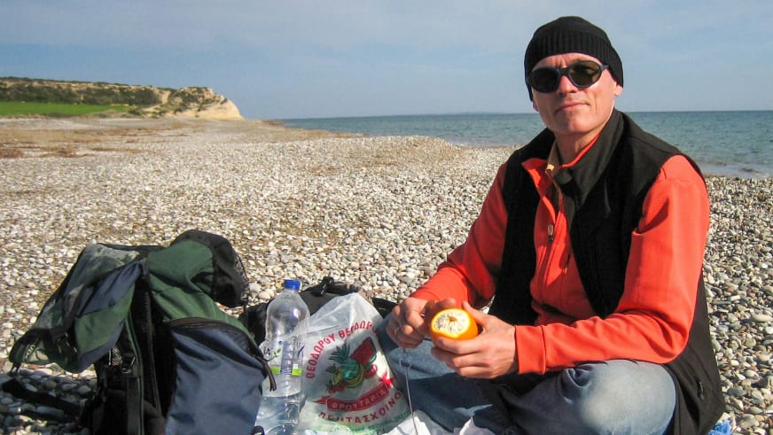 Am Kiesstrand macht Bergwanderführer Reinald Zölch Pause und hält eine Orange in den Händen.