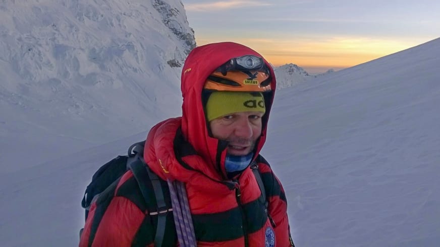 Bei Sonnenuntergang trägt Bergführer Franz Hölzl eine rote Daunenjacke mit Kapuze und eine gelbe Stirnlampe am Kopf.