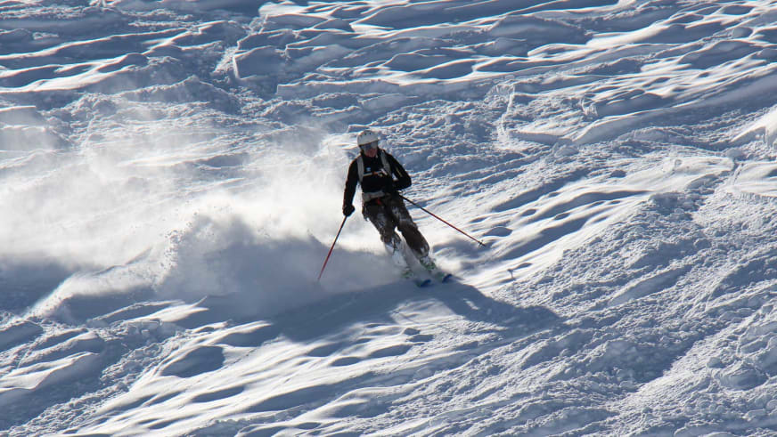 Auf Skiern fährt Bergführer Franz Hölzl einen steilen, verschneiten Hang hinab und wirbelt Pulverschnee auf.