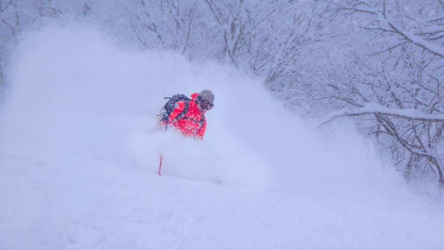 Bergführer Franz Hölzl in roter Winterjacke fährt durch tiefen Pulverschnee und wirbelt eine große Schneewolke auf.
