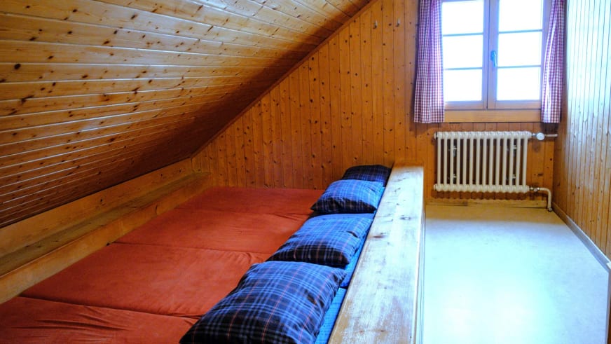 Schlafraum der Vermigelhütte mit Holzpritschen, roten Matratzen und karierten Kissen im Dachgeschoss.