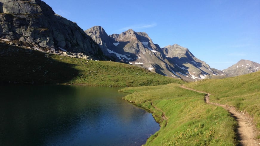 Maighelssee mit Wanderweg am Ufer, umgeben von grünen Almwiesen und Felswänden nahe der Vermigelhütte.