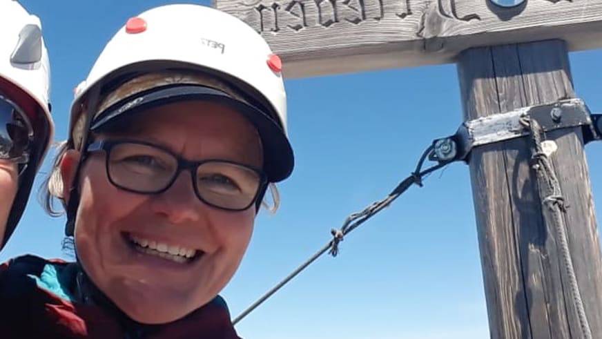 Bergwanderführerin Simone Thater trägt weißen Helm und roten Pullover bei einer Bergtour mit Drahtseil-Konstruktionen.